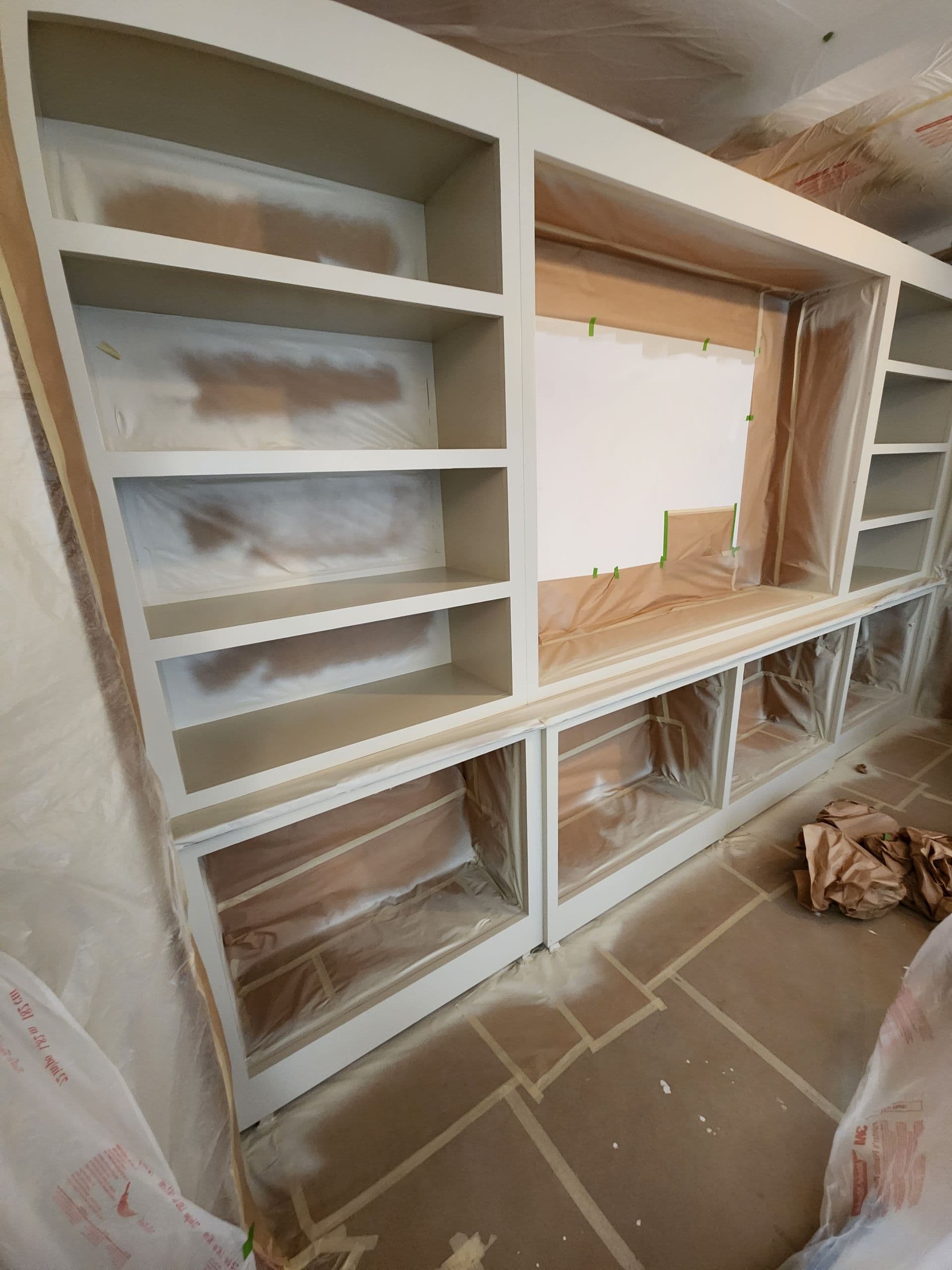 Floor-to-ceiling built-in shelving spray-painted crisp white, with surrounding surfaces carefully masked.
