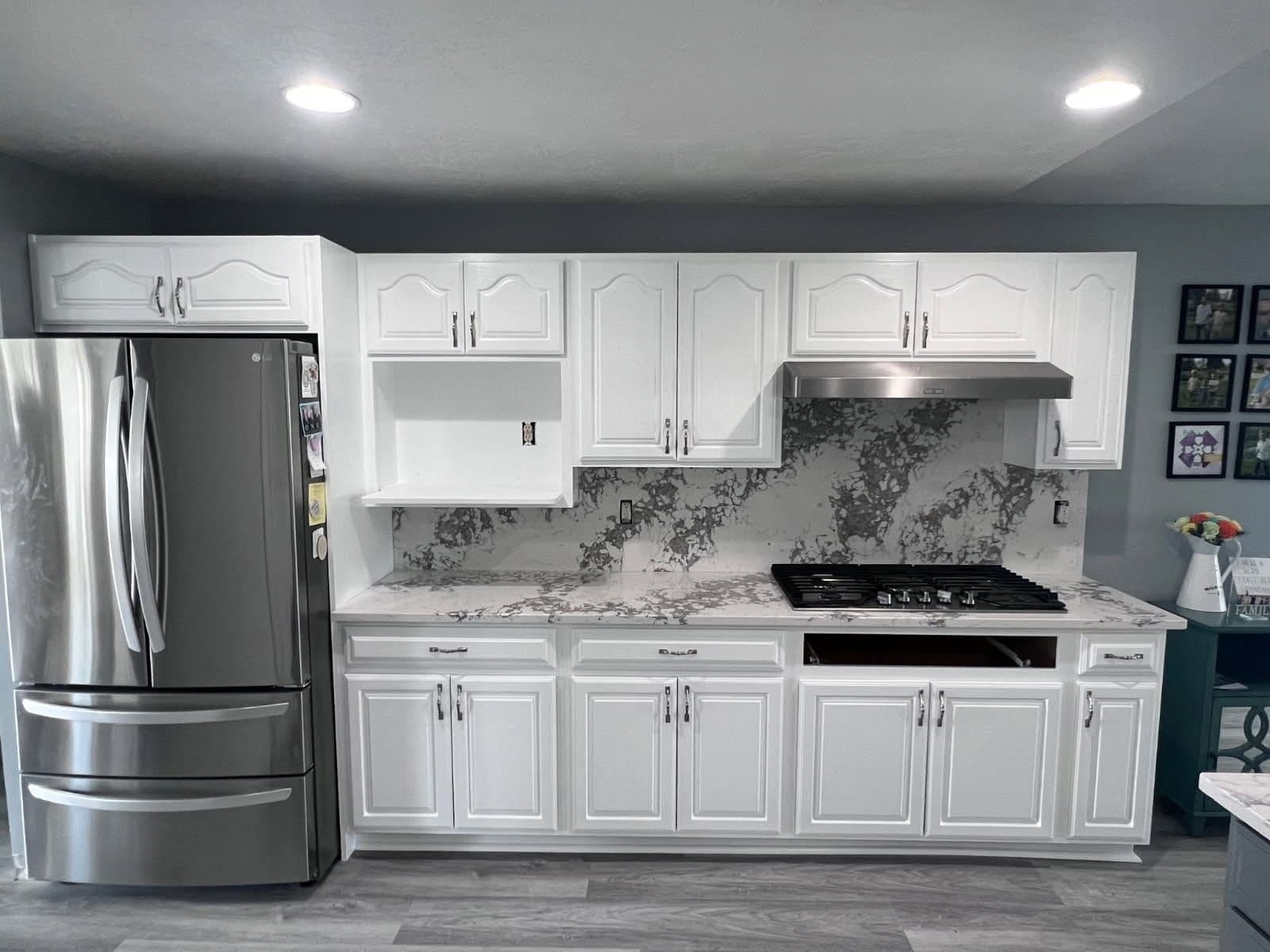 Kitchen cabinets refinished in bright white paint beside a marble backsplash and stainless refrigerator.