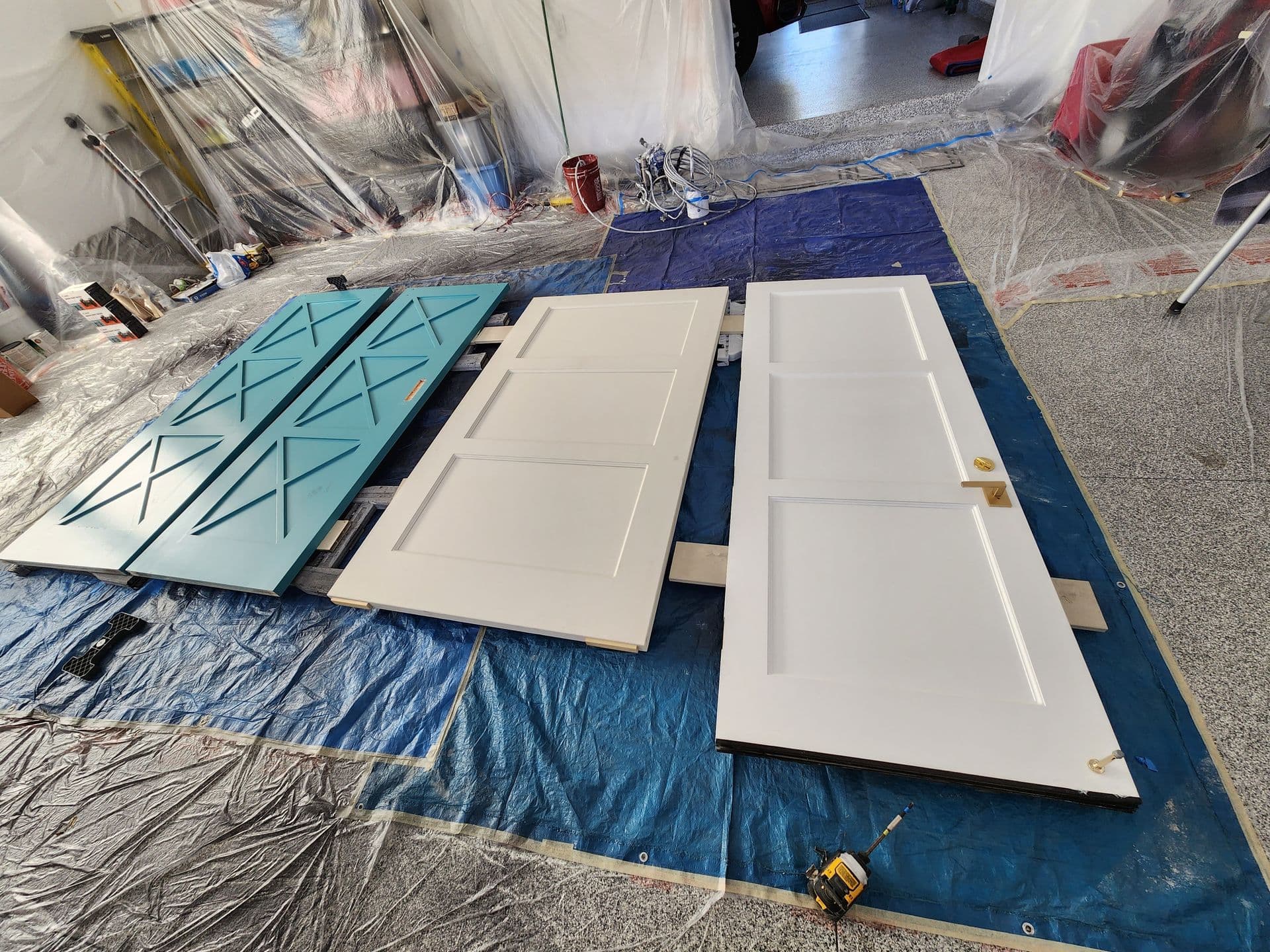Interior doors and a teal barn door spray-finished in a masked garage paint booth.