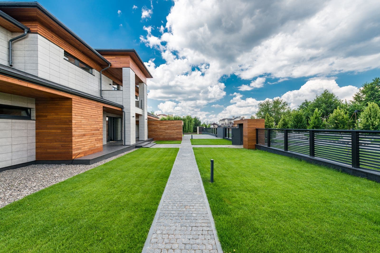 Modern two-story home exterior with wood siding, a painted fence, and a green summer lawn.